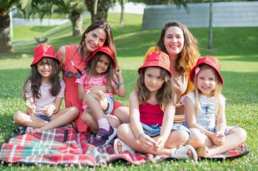 Friends enjoying a sunny day picnic on grass with bucket hats and smiles in a Portuguese park.